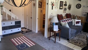 A living room with a grey sofa, a coffee table, and a lamp. There is a staircase leading to another room.