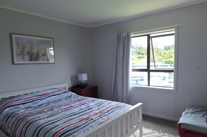 A bedroom with a bed, a nightstand, a window with curtains, and a framed picture on the wall. - Cozy Pet-Friendly Bach – Relax, Unwind or go Fishing! (Kawhia)