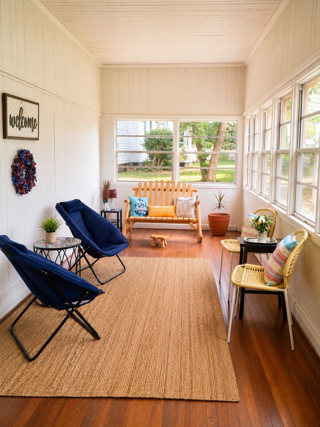 Une pièce baignée de lumière, avec un plancher en bois, une chaise bleue, un fauteuil en osier et un banc agrémenté de coussins.