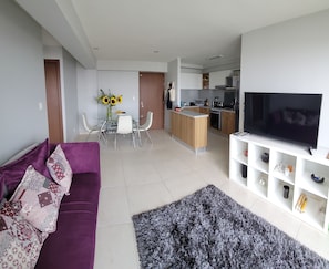 A modern living room with a purple sofa, a grey shag rug, and a TV on a white stand.