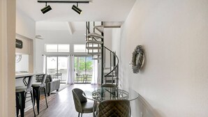 Ein modernes Interieur mit einem Glastisch, schwarzen Stühlen, einer Wendeltreppe und großen Fenstern.