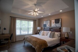 Relax in comfort with a large bed, bedside tables, and a ceiling fan, surrounded by artwork and natural light.