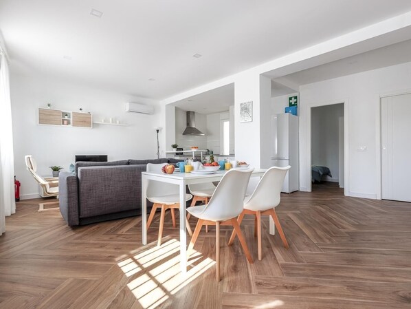 A modern, open-plan living space with a dining area, sofa, and kitchen.