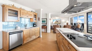 A modern kitchen with wooden cabinets, a dishwasher, and a large island with a stove. - Sea Gull #905LK: Beachfront 2 Bedroom 2 Bathroom With Spectacular Views and 24 Hour Management (Port Aransas)