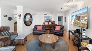 A living room with a round coffee table, two sofas, and a television on the wall. - Sea Gull #905LK: Beachfront 2 Bedroom 2 Bathroom With Spectacular Views and 24 Hour Management (Port Aransas)