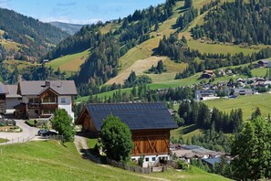 Un pittoresco villaggio rurale caratterizzato da case in legno tradizionali, un fienile dotato di pannelli solari e una strada tortuosa.