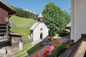 A small church with a bell tower, surrounded by greenery and a wooden building. - Apartment 'Paracia Pec' with Access to Ski Slopes, Mountain View, Balcony & Wi-Fi (Badia)