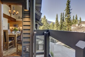 Een moderne keuken met houten kasten, een eethoek met een houten tafel en stoelen, en uitzicht op een bebost berglandschap.