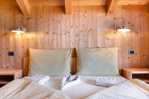 Una habitación tipo cabaña de madera con una cama, dos mesitas de noche y luces fijadas a la pared.