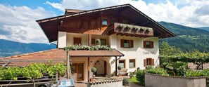 Un bâtiment à deux étages, doté d’un toit en pente, d’un balcon orné de plantes et offrant une vue sur les montagnes.