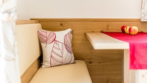 A wooden bench with a cushion, a small table with a red cloth, and two apples on the table. - Holiday Apartment 'Rasnerhof Ferienwohnung Talblick' with Mountain View, Balcony & Wi-Fi (Algund)