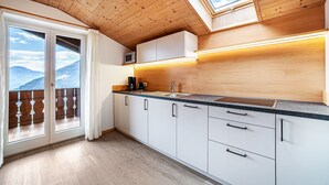 Eine moderne Küche mit Holzboden, weißen Schränken, einer schwarzen Arbeitsplatte und Blick auf Berge durch große Schiebetüren.