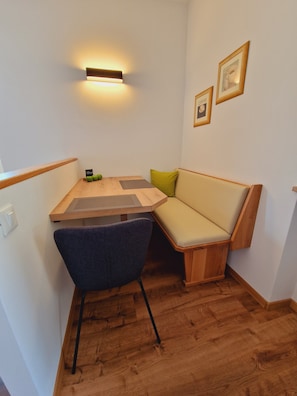 A compact room with a wooden table, a cushioned bench, a chair, and a wall-mounted light fixture.