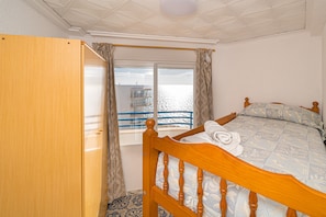 Een slaapkamer met een houten bed, een raam met gordijnen en uitzicht op zee.