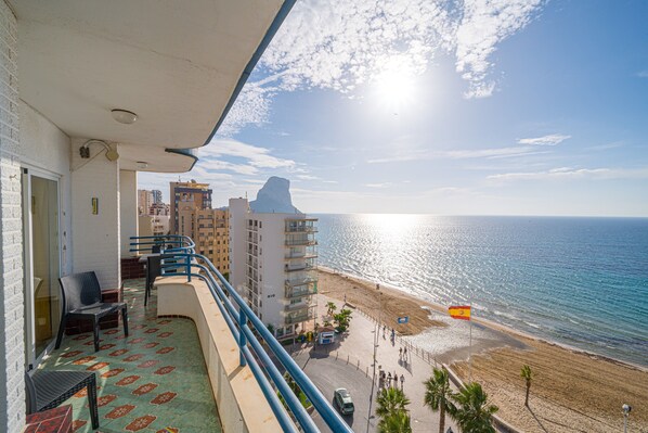 A balcony with a view of the beach and ocean, a flag, and a building with balconies. - Apto en Primera Línea Arenal Calpe with Sea View, Terrace & Wi-Fi (Calpe)