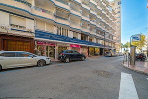 Een straatgezicht met een rij winkels, waaronder een pedicure salon, en een meerlaags gebouw met balkons.