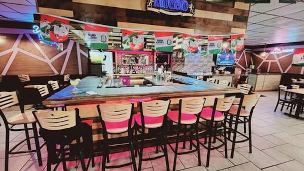 A bar area with a long counter and multiple stools. - Roadside Inn (Osceola)