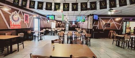 Un restaurante espacioso con varias mesas y sillas, un escenario al frente y pancartas de Guinness en el techo.