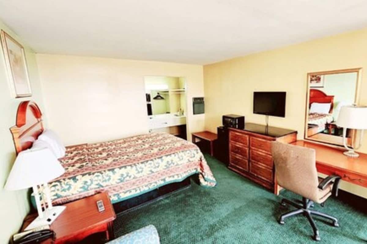 Ein Hotelzimmer mit Bett, Schreibtisch, Stuhl, Kommode, Fernseher und Spiegel.