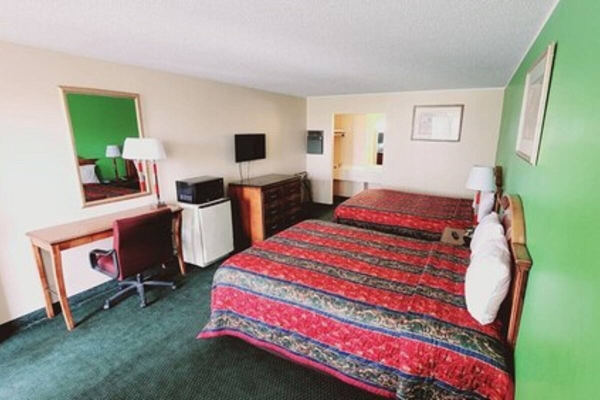 Ein Hotelzimmer mit einem Bett, einem Schreibtisch, einem Sessel, einer Kommode, einem Fernseher und einer grünen Wand.