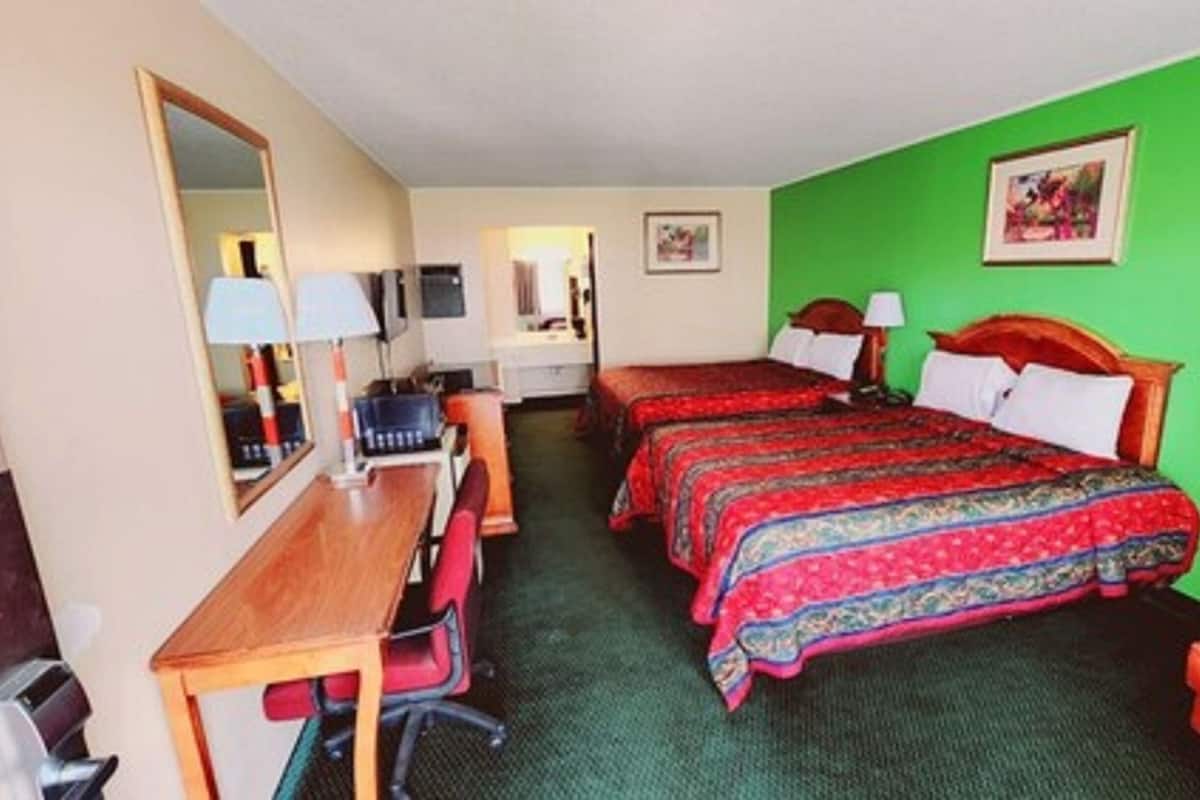 Ein Hotelzimmer mit zwei Betten, einem Schreibtisch, einem Stuhl und einem Spiegel.