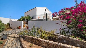 A white building with a stone wall and a metal fence, surrounded by potted plants and flowers. - Pet-Friendly Villa 'Casa dos Jotas' with Pool & Wi-Fi (Martinlongo)