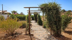 A stone pathway leading through a garden with a wooden pergola structure. - Pet-Friendly Villa 'Casa dos Jotas' with Pool & Wi-Fi (Martinlongo)
