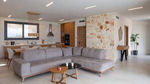 A modern living room with a grey sectional sofa, a round coffee table, and a kitchen area with a stone accent wall.