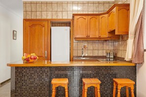 A kitchen with wooden cabinets, a tiled backsplash, a refrigerator, and two stools.