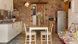 Une cuisine aux murs en pierre, une table en bois avec deux chaises, un four à micro-ondes et un canapé agrémenté de coussins à motifs.