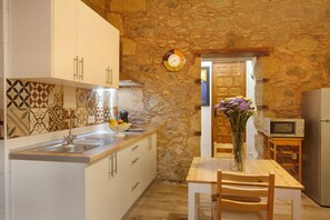 Une cuisine avec des murs en pierre, un évier, des placards, un four à micro-ondes et une table à manger avec des chaises.