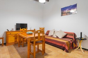 Une petite pièce agréable, dotée d’un lit, d’une table avec des chaises, d’un téléviseur et d’un tableau accroché au mur.
