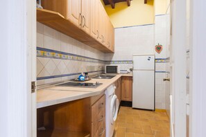 Une cuisine compacte avec des meubles de rangement en bois, un lave-linge, un four à micro-ondes et un réfrigérateur.