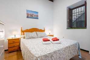 Une chambre à coucher avec un lit en bois, deux tables de chevet avec des lampes, une fenêtre donnant sur un beau paysage et un tableau représentant une vue de la ville accroché au mur.