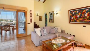 Un salon comprenant un canapé, une table basse en verre, un coin repas avec des chaises et une table, et une vue à travers une porte vitrée.
