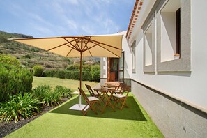 Un patio con mesa y sillas, una sombrilla grande y vistas a una colina.