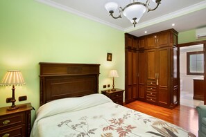 Un dormitorio con cama, armario de madera, mesitas de noche, lámparas y una araña.