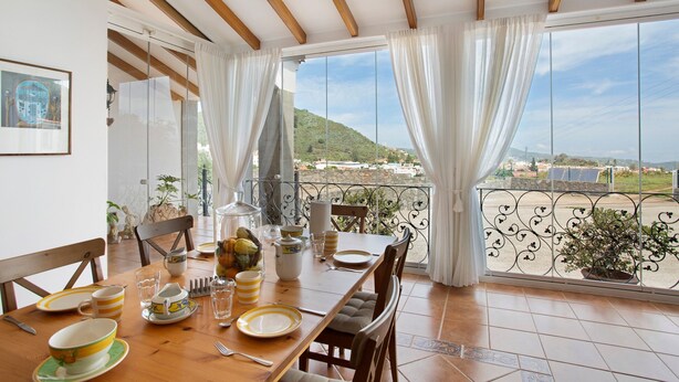 Un coin repas avec une table dressée pour quatre personnes, un balcon avec vue et une plante en pot.
