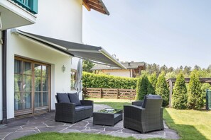Een terras met rieten meubilair, een stenen vloer en uitzicht op een bebost gebied.