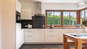 Ett modernt kök med vita skåp, en svart bänkskiva, en rostfri köksfläkt och ett stort fönster med utsikt över grönområden.
