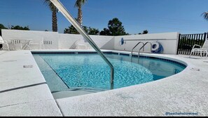 A swimming pool with a metal ladder, white tiled deck, and a white wall with a blue logo.