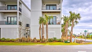 A modern multi-story building with balconies, palm trees, and a street view.