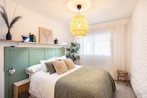 A neatly arranged bedroom with a bed, bedside table, lamp, and a hanging light fixture.