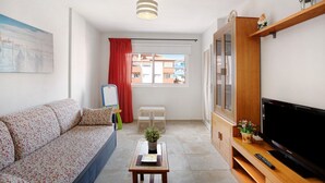 A living room with a sofa, a small table, a TV, and a window with a view of buildings. - Vacation Apartment 'Puertito Guimar' with Shared Terrace, Balcony and Wi-Fi (Guimar)