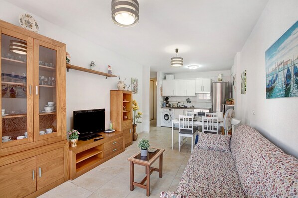 A living room with a TV, wooden cabinets, a sofa, and a small table with a plant.