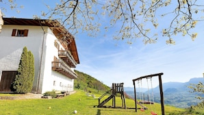 Ein weißes Gebäude mit einem hölzernen Balkon, einer Schaukel und freiem Blick auf die Berge.