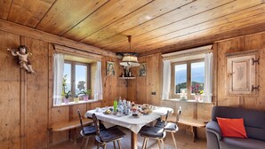 A wooden interior with a dining table, chairs, a sofa, and windows with views.