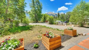 Un jardín con jardineras de madera, un camino de grava y una montaña al fondo.