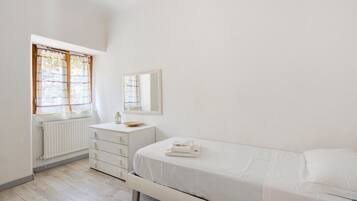 Une chambre à coucher comprenant un lit, une commode, un miroir, un radiateur et une fenêtre avec des rideaux.