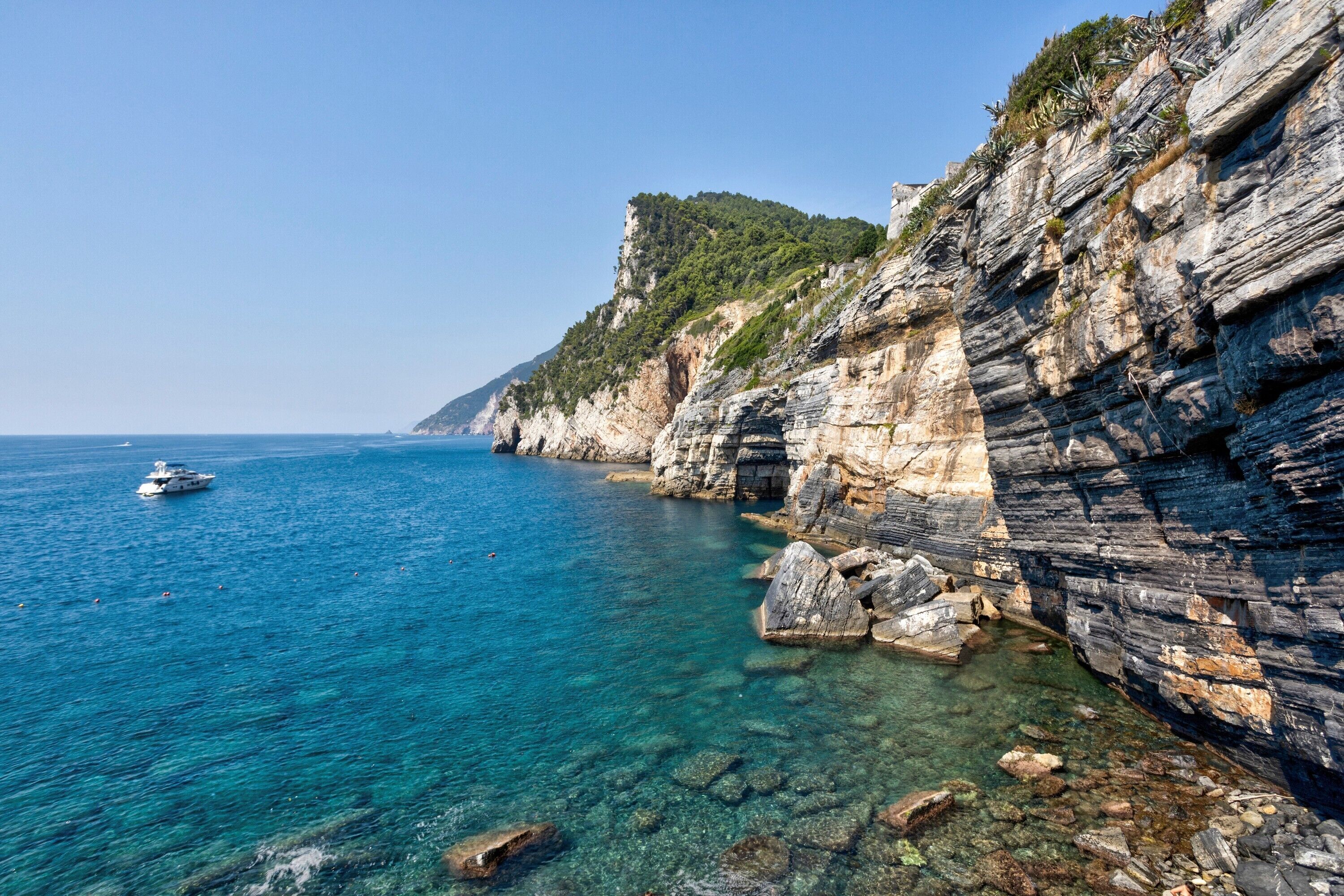 A coastal landscape with clear water, rocky cliffs, and a boat.